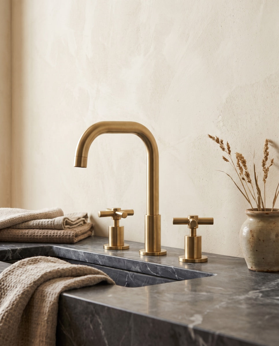 A widespread brushed-brass bathroom faucet on a honed stone vanity in the ANVE showroom.