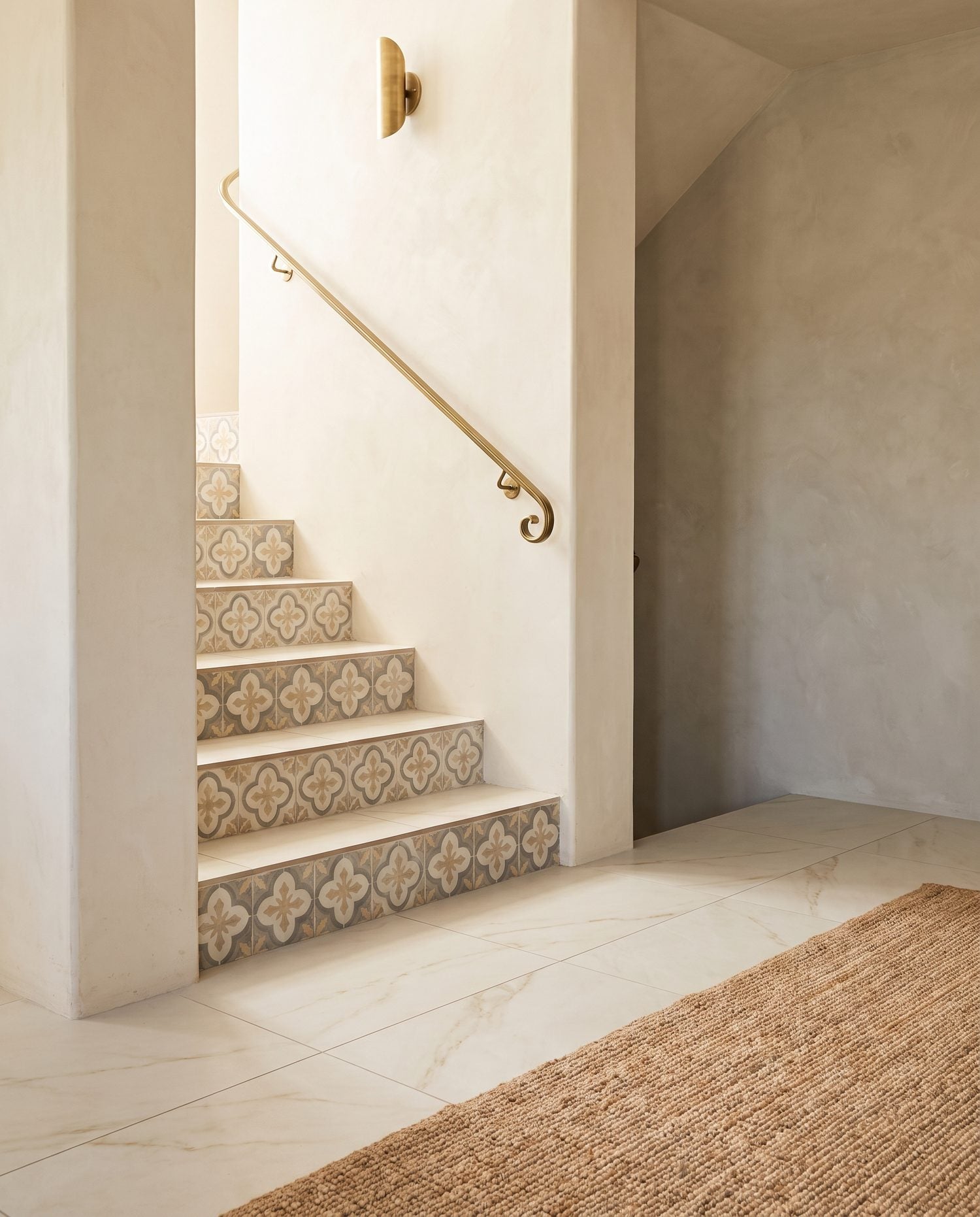 The bottom of a tiled staircase meeting a matte porcelain floor, with decorative tile risers, in the ANVE style.