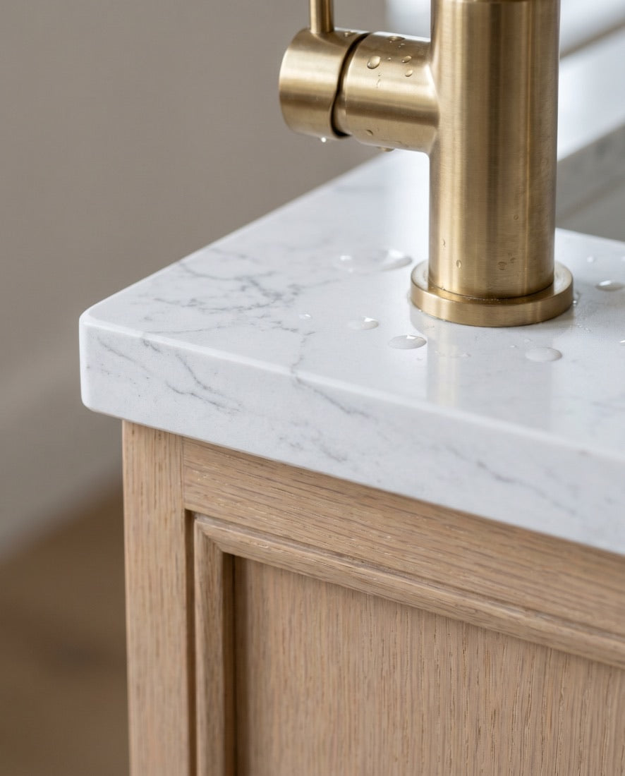 A 3 centimeter honed marble-look quartz vanity top meeting a white-oak cabinet with a brushed-brass faucet.