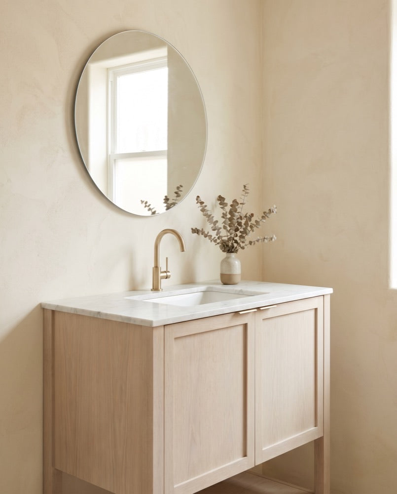A compact white-oak bathroom vanity with a honed marble top and brushed-brass faucet.