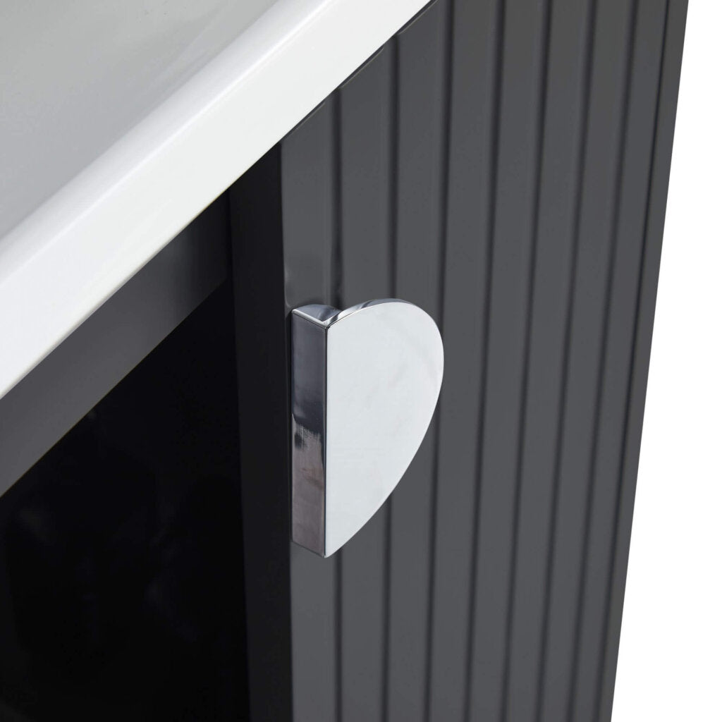 A close-up of a cabinet with vertical grooves, a shiny heart-shaped chrome handle, and part of a white countertop above, from the elegant Venezian 24 inch Bathroom Vanity With Sink.