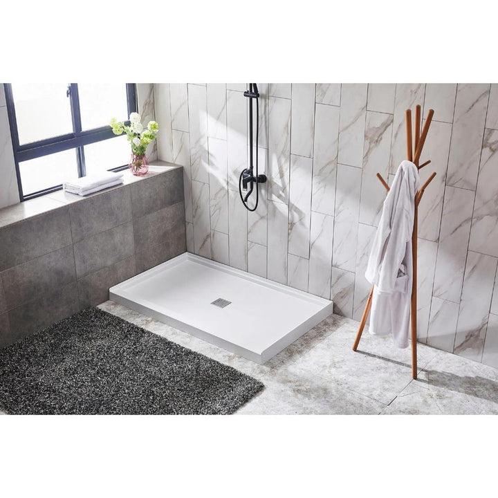 A modern bathroom features a Bhavana Single Threshold Shower Base, black shower fixture, marble wall tiles, a large window with a potted plant, a dark textured rug, and a wooden coat rack with a white robe.
