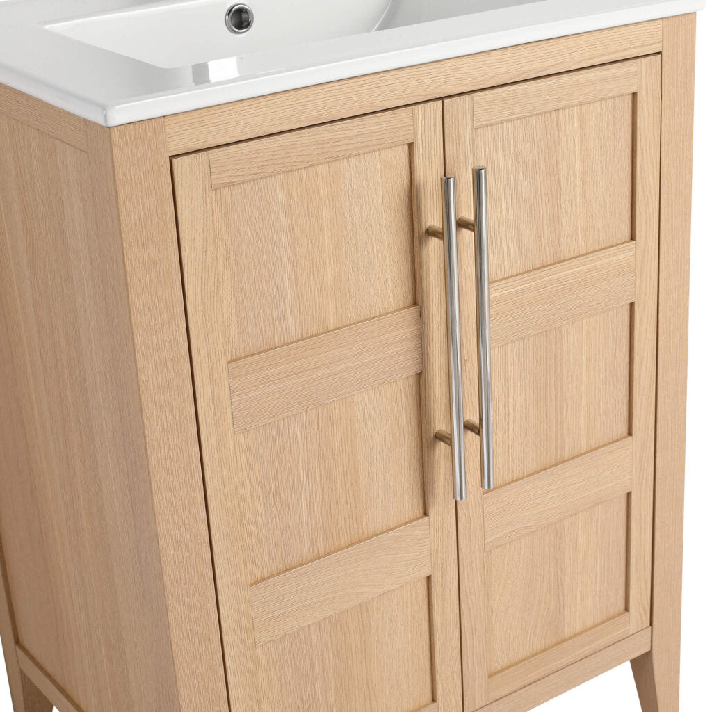 The Leafside 24 Inch Bathroom Vanity With Sink features a wooden frame and white sink, complemented by two paneled doors with vertical metal handles in a light, natural finish.