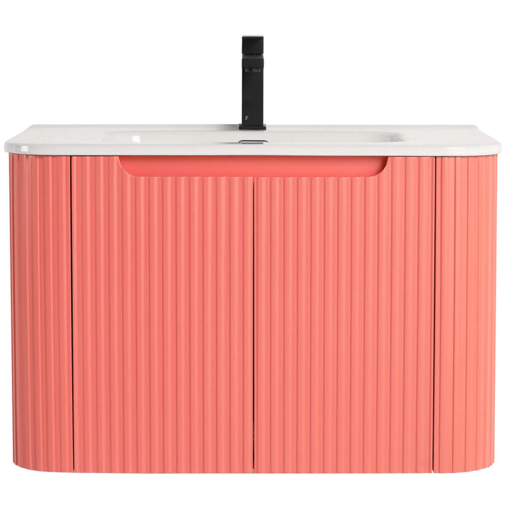 The Caskvalley 30 Inch Wall Mounted Bathroom Vanity boasts a ribbed coral pink cabinet and white countertop, paired with a single black faucet and integrated sink. Its handle-free design provides a sleek, minimalist look.