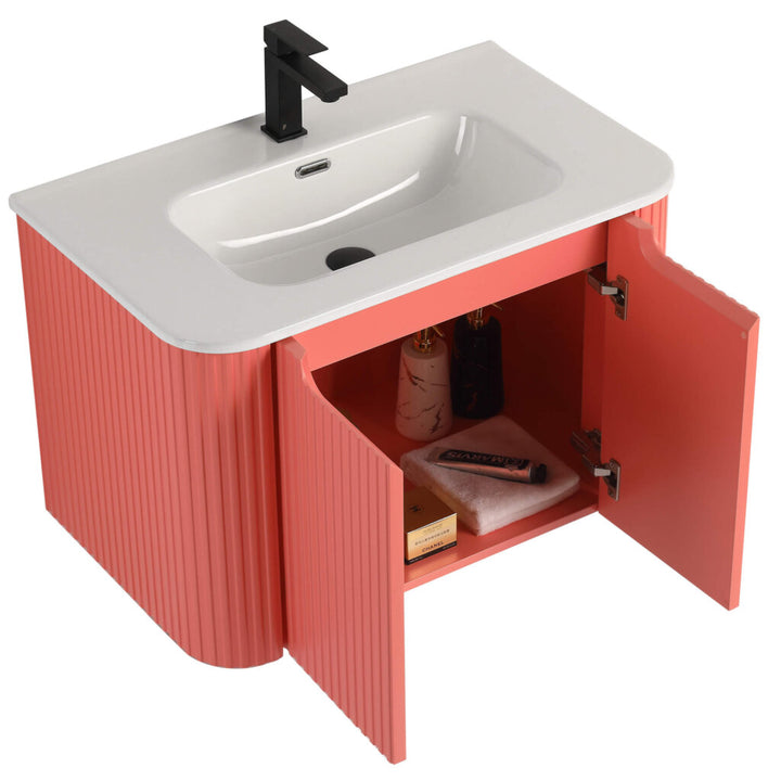 Discover the Caskvalley 30 Inch Wall Mounted Bathroom Vanity With Sink, marrying elegance and utility; a white sink paired with a black faucet sits on coral-textured cabinets, highlighted by open doors displaying neatly organized bottles and towels.