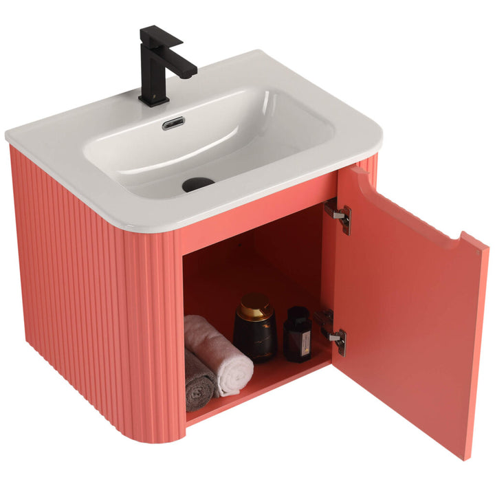 The Caskvalley 24 Inch Wall Mounted Bathroom Vanity With Sink features a coral color with a white sink and black faucet. An open cabinet door reveals rolled towels and dark bottles, while ribbed side textures enhance its elegance.