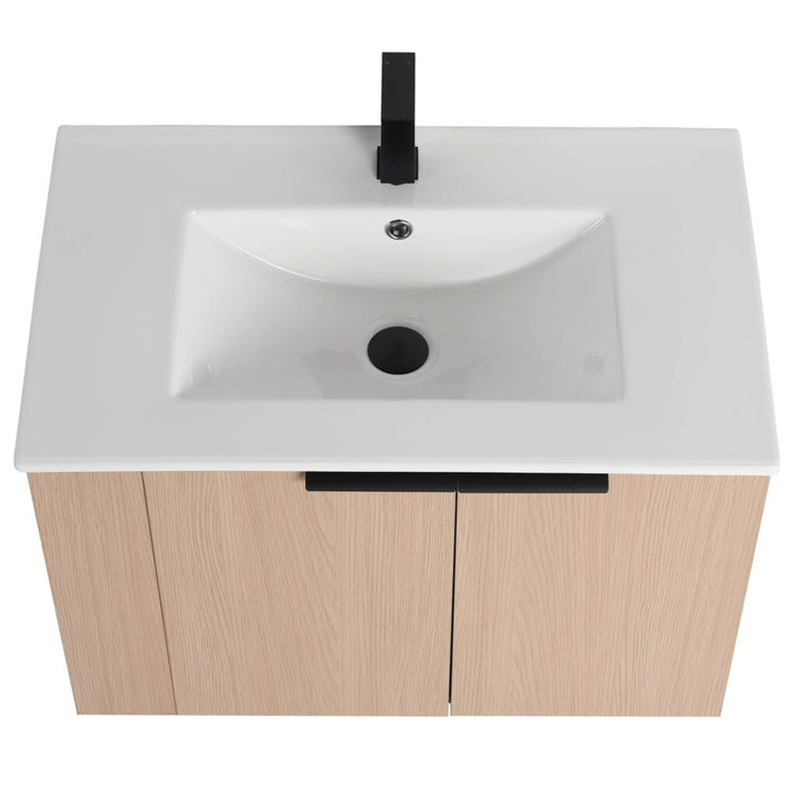The Elmridge 30 Inch Wall Mounted Vanity features a modern design with a light wood cabinet, rectangular white ceramic sink, black faucet, central drain, and overflow hole. The striking black faucet contrasts beautifully with the light wood and pristine sink.
