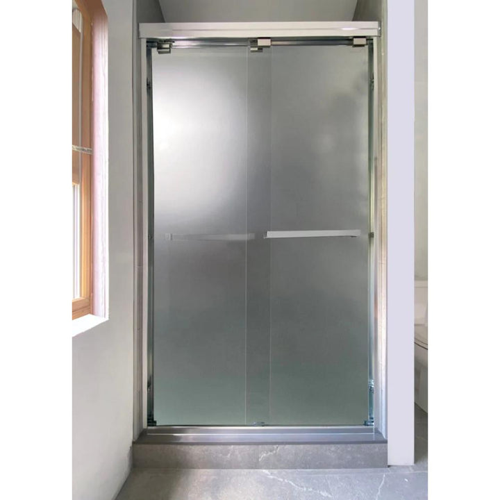 A modern bathroom showcases the ASD Cascade Shower Door – Bypass Sliding with a frosted glass panel and sleek metal frame, set beside a window with wooden trim that floods the space with natural light.