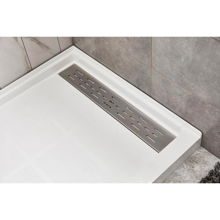 Close-up of a Bhavana Single Threshold Shower Base with large, light tiles and a rectangular stainless steel linear drain, framed by gray and marble-patterned wall tiles for a sleek, modern appearance.