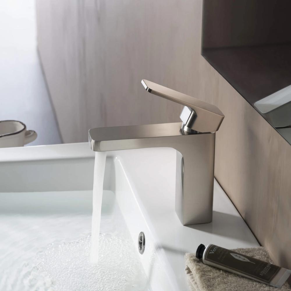 The Fusion Single Handle Bathroom Vanity Sink Faucet pours water into a white sink. Nearby are a towel and small tube, with the edge of a mirror and an additional container visible in the background.