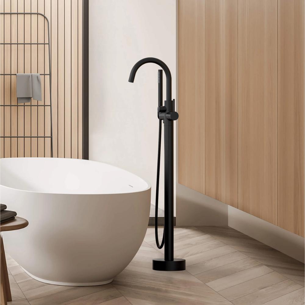A modern bathroom with a white freestanding tub, the Halo Floor Mount Tub Filler With Hand Shower in black, light wood panel walls, and a geometric tile floor.
