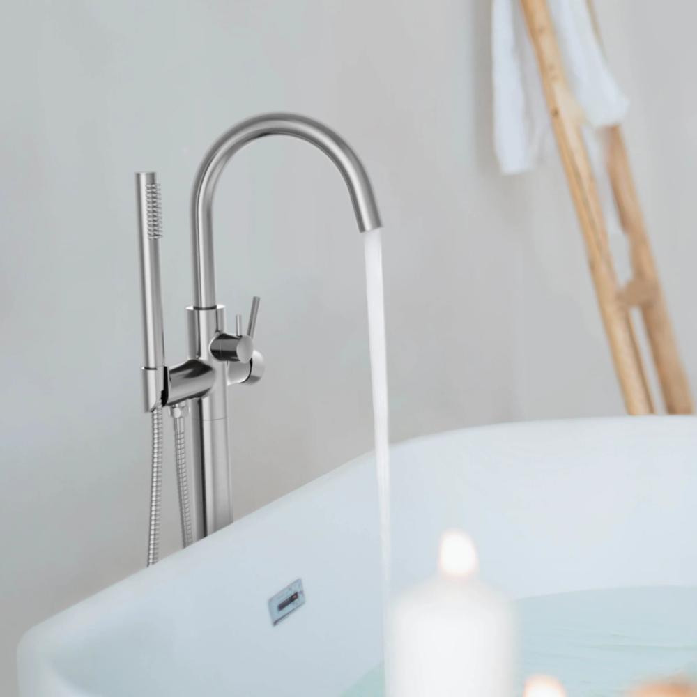 The Halo Floor Mount Tub Filler With Hand Shower stands by a white tub, while a wooden ladder with a towel and a glowing candle help create a tranquil, spa-like setting.