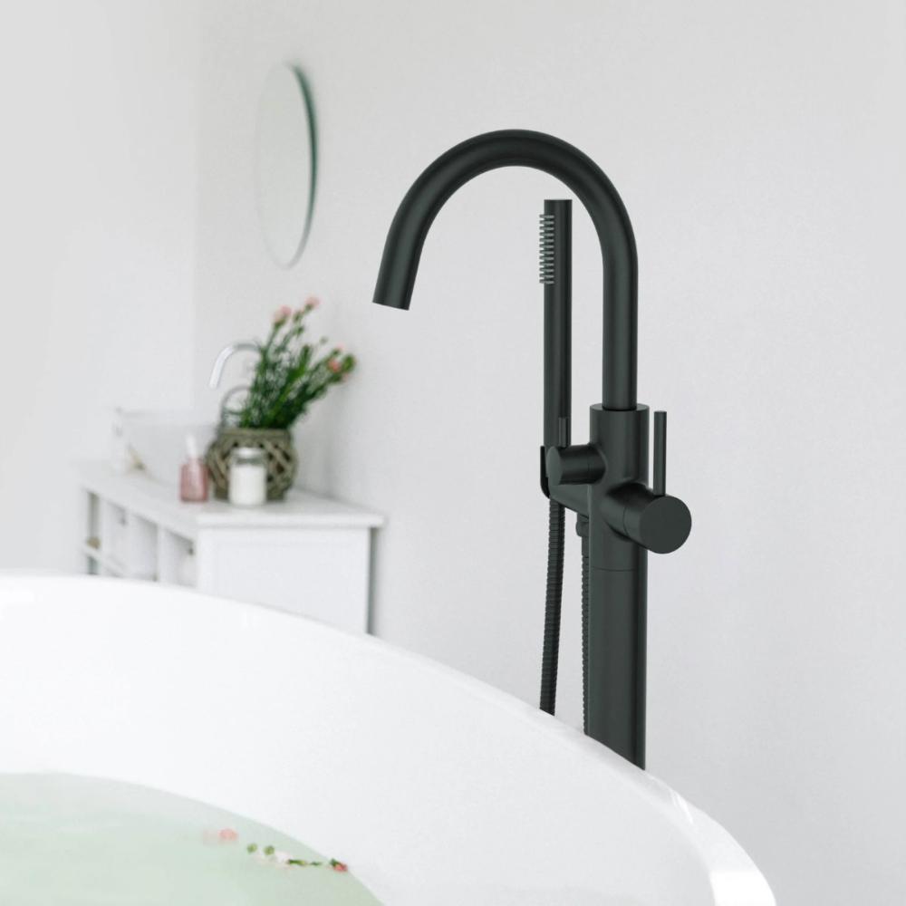 The Halo Floor Mount Tub Filler With Hand Shower in matte black features a curved spout beside a white bathtub in a modern, minimal bathroom, with a vanity and mirror visible in the background.