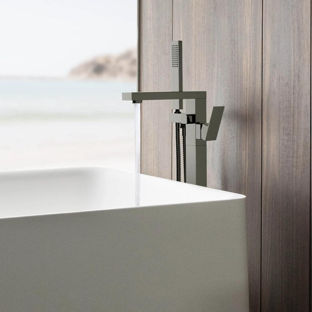 The Quadra Floor Mount Tub Filler With Hand Shower in chrome fills a white bathtub set by a wooden wall, while a blurred beach view appears outside.