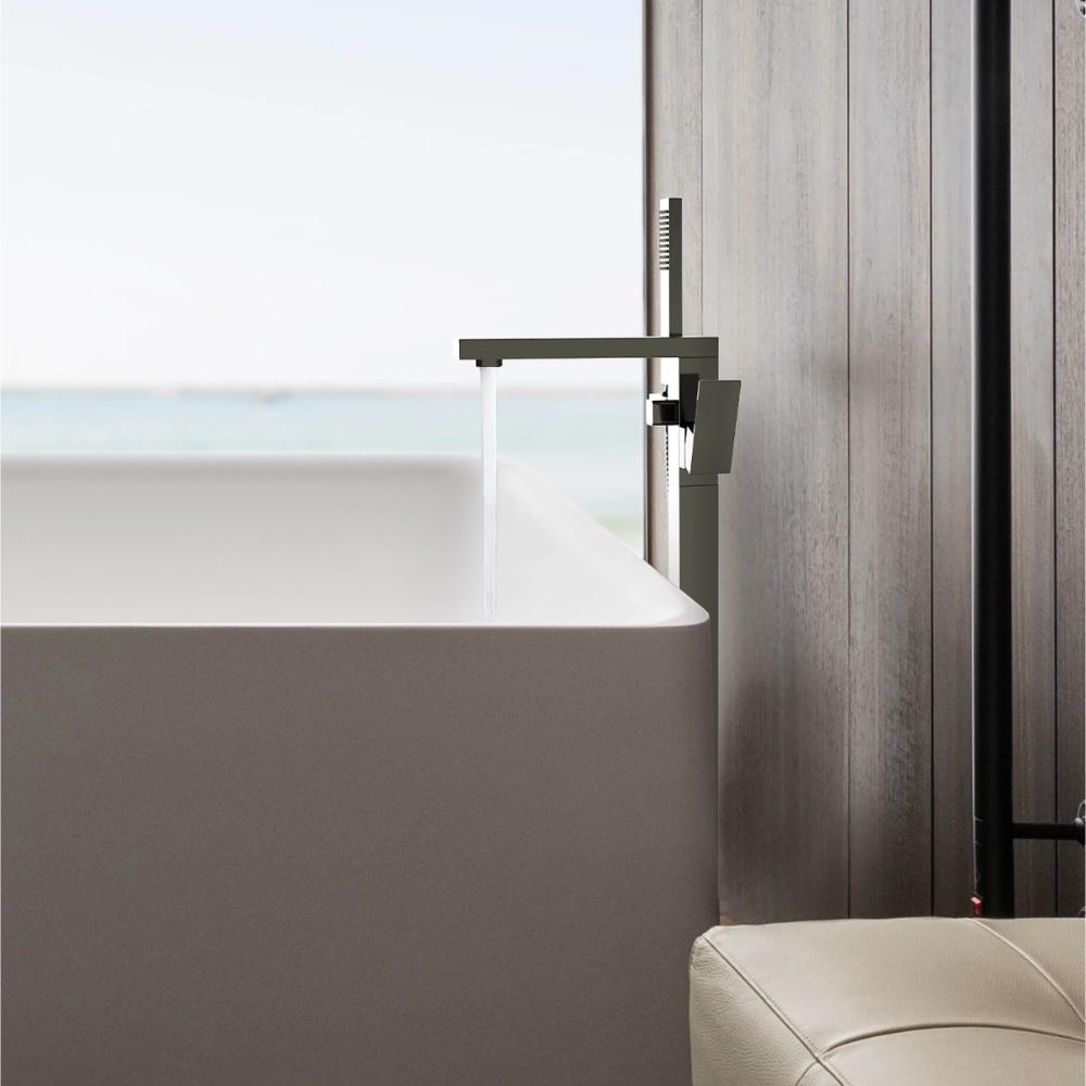 A modern bathroom features a white bathtub with the Quadra Floor Mount Tub Filler With Hand Shower in sleek black, light wood walls, ocean views through a large window, and a beige cushioned seat in the foreground.