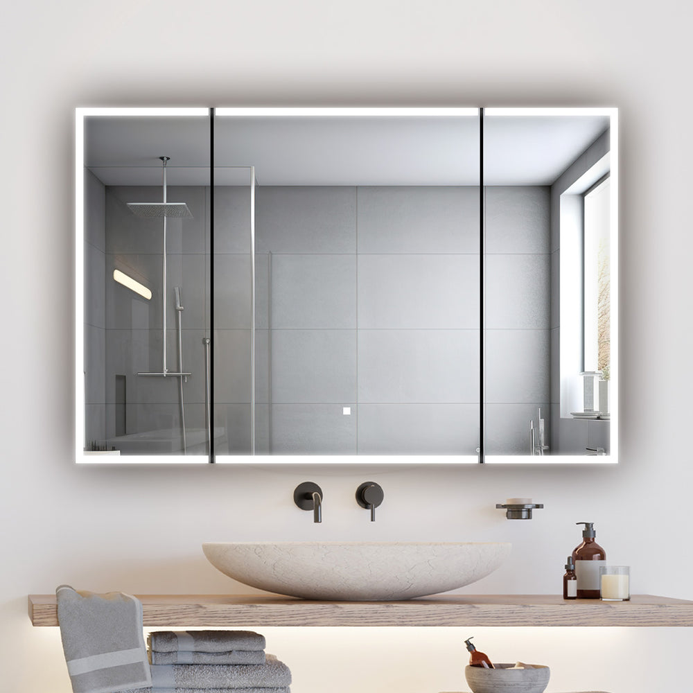 A modern bathroom features a round stone sink on a wooden counter, folded towels, and toiletries. An Edge Royal 48 Inch LED Lighted Mirror 3 Door Medicine Cabinet serves as a large mirror, reflecting the shower with gray tiles and a window.