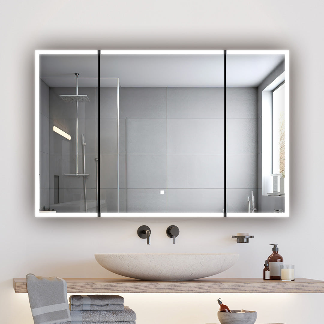 A modern bathroom features a round stone sink on a wooden counter, folded towels, and toiletries. An Edge Royal 48 Inch LED Lighted Mirror 3 Door Medicine Cabinet serves as a large mirror, reflecting the shower with gray tiles and a window.