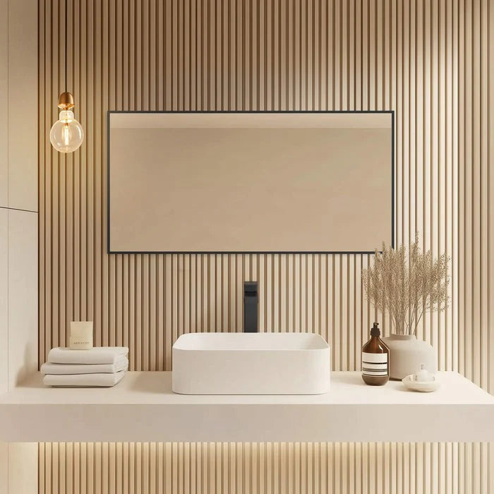 A modern bathroom showcases Metal Framed Mirrors above a floating vanity with a rectangular white sink, stacked towels, bottles, a vase with dried plants, a wall sconce, and vertical wood slat paneling.