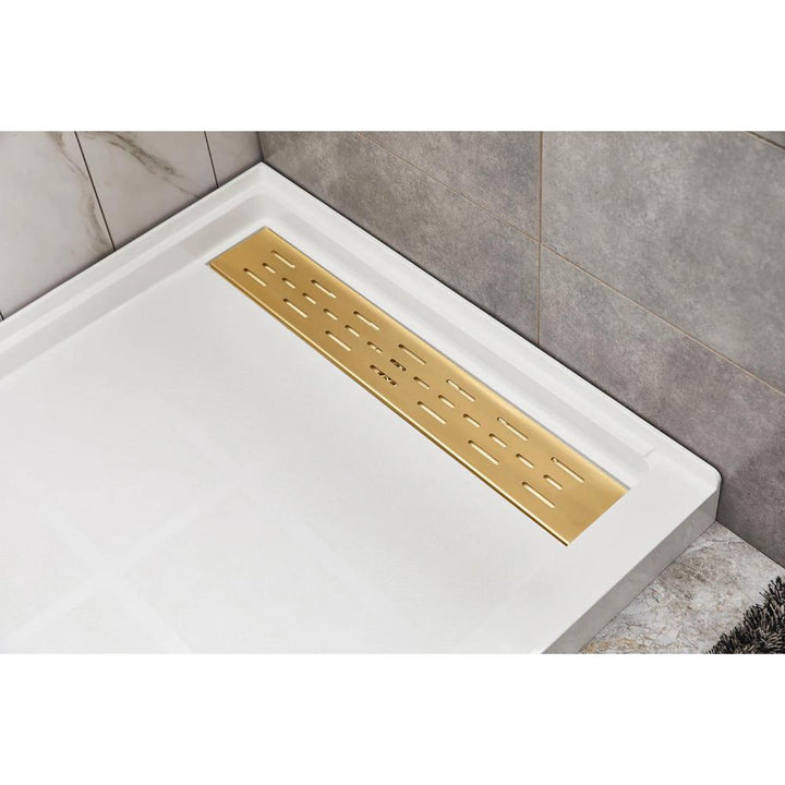 A modern shower floor showcases the Bhavana Single Threshold Shower Base and a rectangular gold-toned linear drain, set against white and gray corner tiles.
