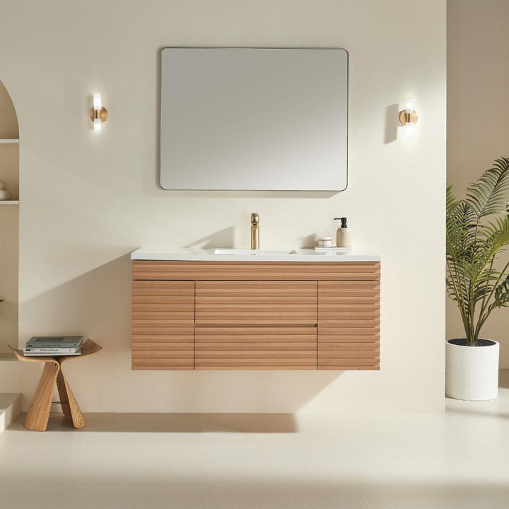 Minimalist bathroom featuring the Linea 48 Inch Wall Mounted Bathroom Vanity, a rectangular mirror, modern brass faucet, two wall sconces, a small wooden stool with books, and a potted plant against a light beige wall.