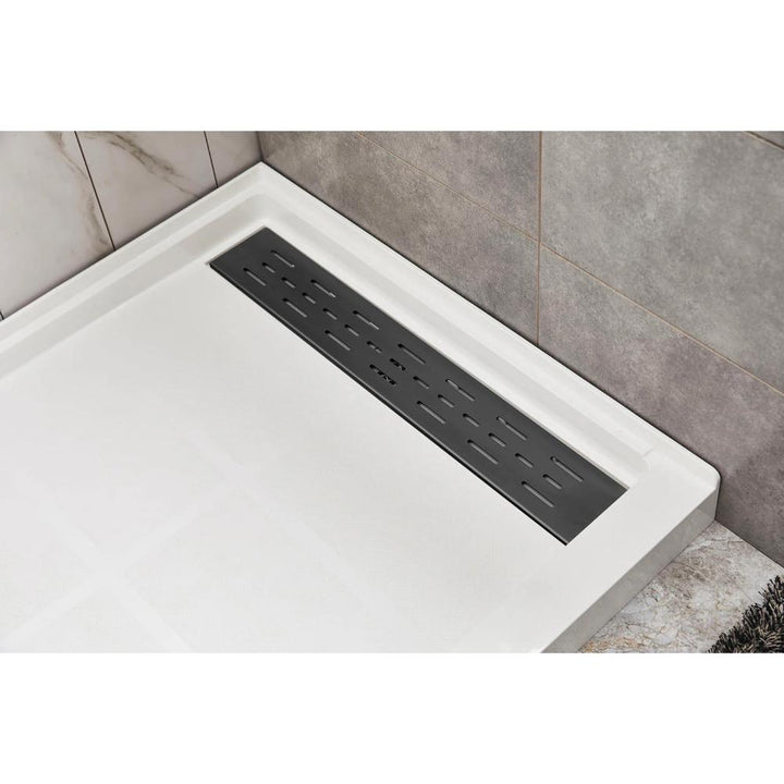 Corner view of a modern Bhavana Single Threshold Shower Base featuring a rectangular metal linear drain cover, set against light and dark gray tiled walls.
