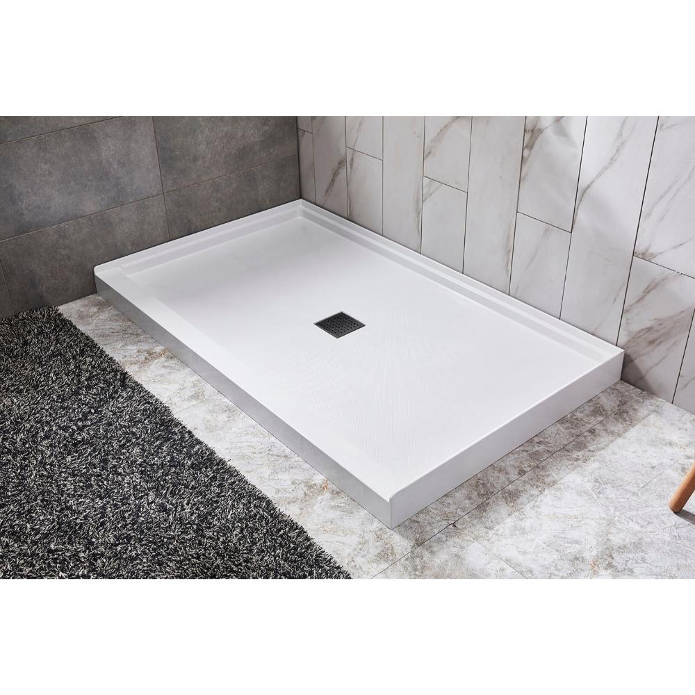 A Bhavana Single Threshold Shower Base, rectangular and white with a centered square drain, is installed against tiled walls and features marble and dark textured flooring.
