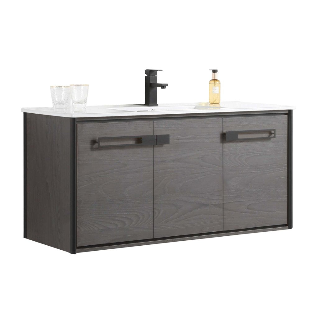 The Oakville 48 inch Modern Bathroom Vanity is wall-mounted with a dark wood finish, three cabinet doors, a white countertop, modern black faucet, two glasses, and a soap dispenser.