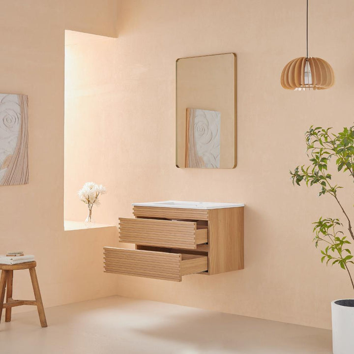 A minimalist bathroom features the Linea 30 Inch Wall Mounted Bathroom Vanity with two drawers open, a rectangular mirror above, a stool on the left, a potted plant on the right, and soft natural light with a vase of white flowers by the window.