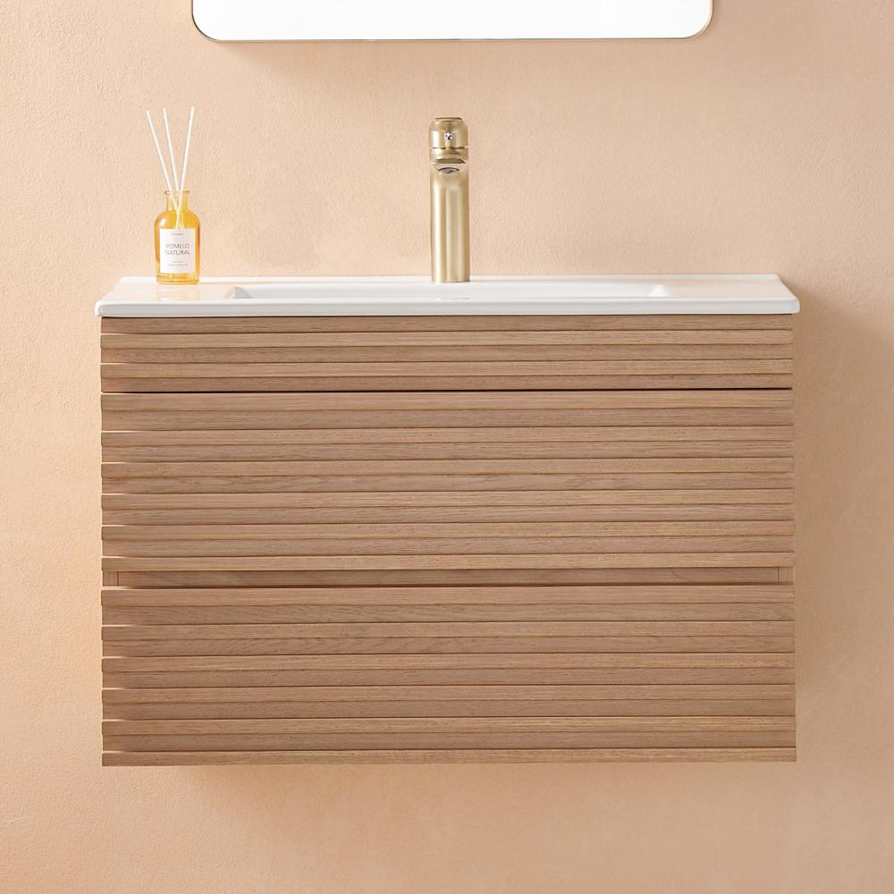 The Linea 30 Inch Wall Mounted Bathroom Vanity has a light wood slatted front, white countertop, gold faucet, and a reed diffuser bottle, all set against a beige wall.