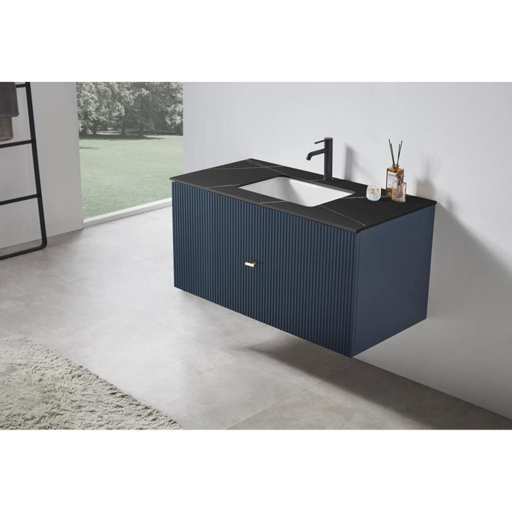 The Barcelona 42 Inch Wall Mount Bathroom Vanity features a ribbed dark blue cabinet, black countertop with integrated sink, and matte black faucet and accessories. A large window offers a view of greenery in the background.
