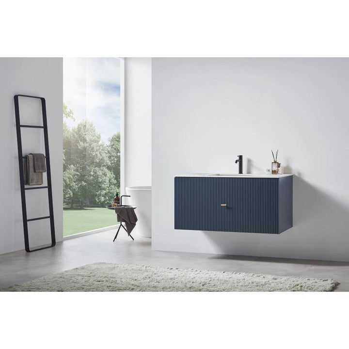 A modern bathroom with a large window, a blue Barcelona 42 Inch Wall Mount Bathroom Vanity with a black faucet, a ladder towel rack, a chair, and a light rug on concrete flooring. Trees can be seen outside.
