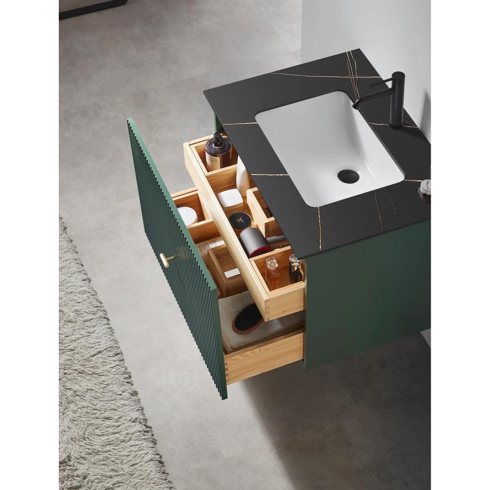 A Barcelona 30 Inch Wall Mount Bathroom Vanity with a black countertop, white sink, green cabinet door, and open wooden drawers holding toiletries sits on a grey floor next to a light textured rug.