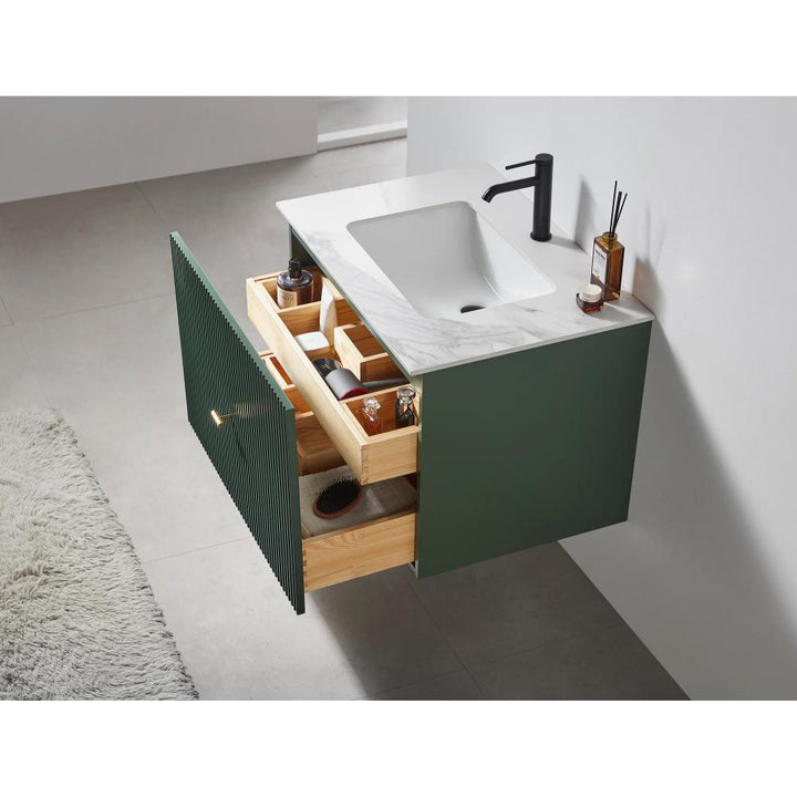 The Barcelona 30 Inch Wall Mount Bathroom Vanity has a white marble countertop, black faucet, green cabinet, open wood drawers with organized toiletries, and a cream rug partly on the floor.