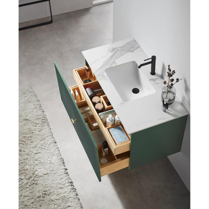 The Barcelona 42 Inch Wall Mount Bathroom Vanity has a white marble countertop, black faucet, and an open wooden drawer with neatly arranged toiletries. A vase with dried flowers and a glass cup rest on the counter, above a plush rug.