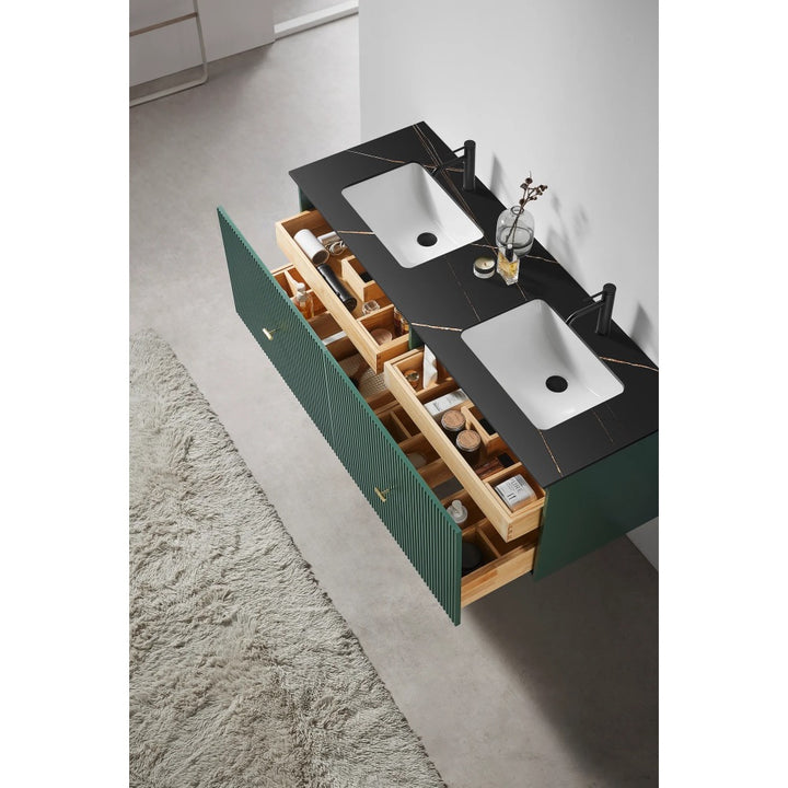 The Barcelona 60 Inch Wall Mount Double Bathroom Vanity With Top features two white square sinks, a black countertop, green cabinets with gold handles, organized open drawers with toiletries, and a beige textured rug on the floor.