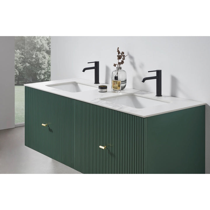 The Barcelona 60 Inch Wall Mount Double Bathroom Vanity With Top features dark green, vertically grooved drawers, a white countertop, two black faucets, and minimal decor. A window offers views of greenery that enhance the vanity’s modern style.