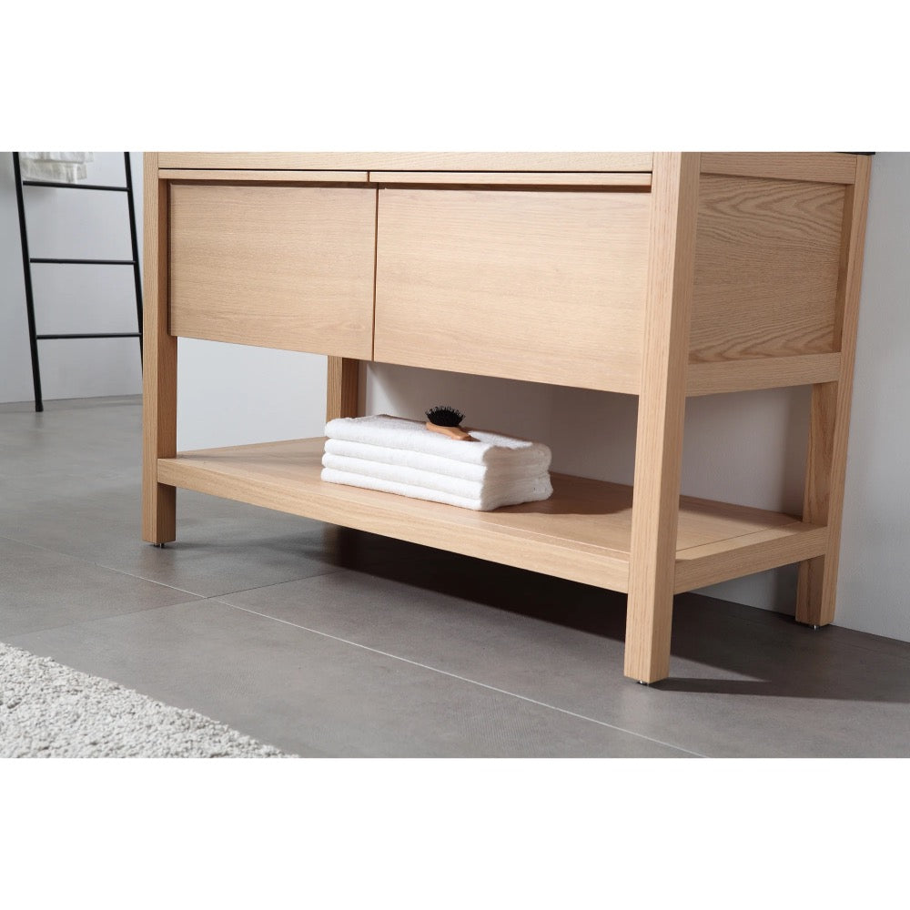 A light wood Bibury 48 Inch Double Bathroom Vanity with Top features two drawers and an open lower shelf with white folded towels and a small black brush, standing on a gray tiled floor beside a light-colored rug.