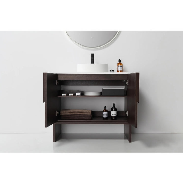 The Celle 36 Inch Bathroom Vanity With Vessel Sink features open dark wood cabinets with shelves for towels and toiletries, plus a round mirror and a white vessel sink with black faucet for a modern touch.