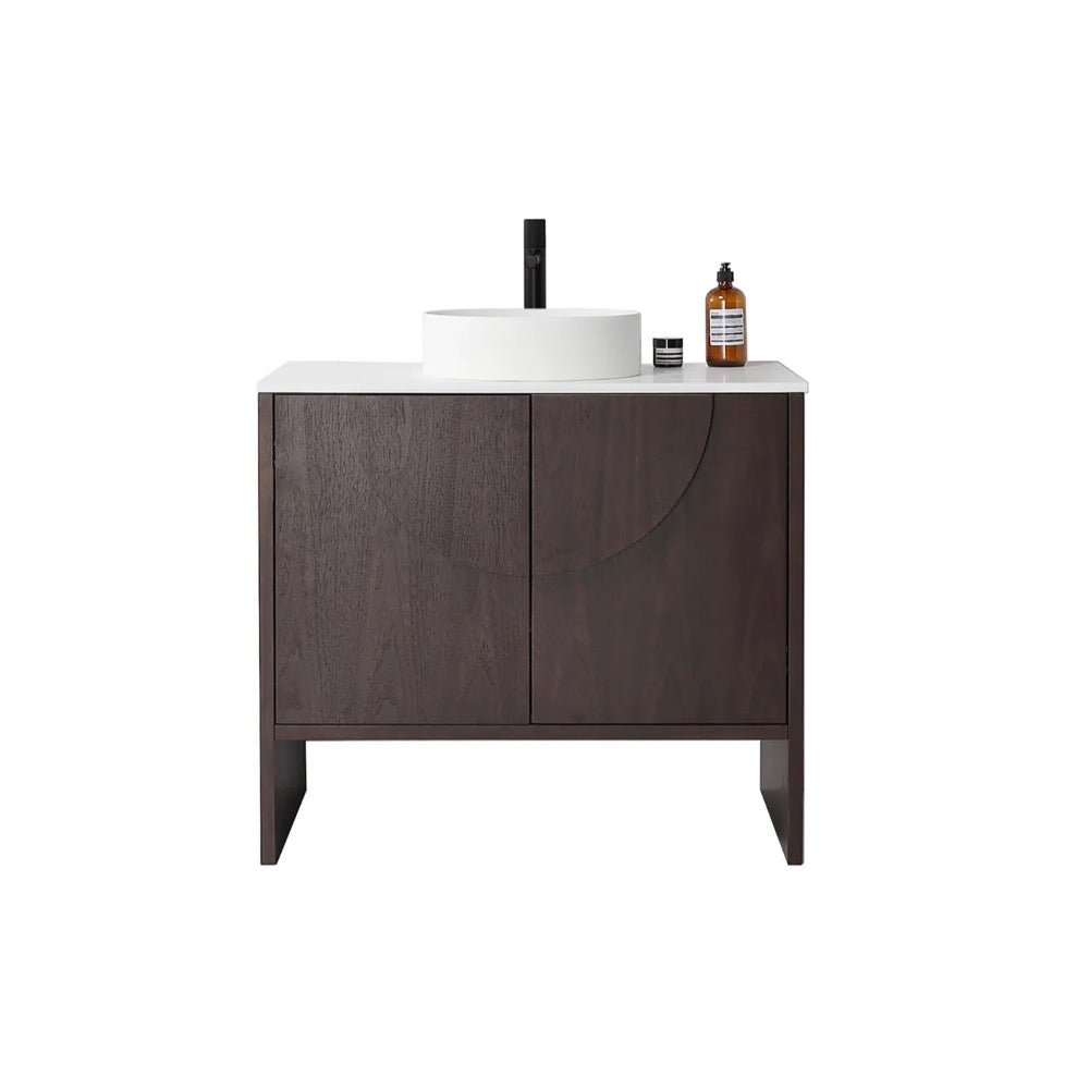 The Celle 36 Inch Bathroom Vanity With Vessel Sink showcases a dark wood cabinet, a white countertop with a round basin, a black faucet, and decorative accents such as a small round container and brown bottle on the right side.