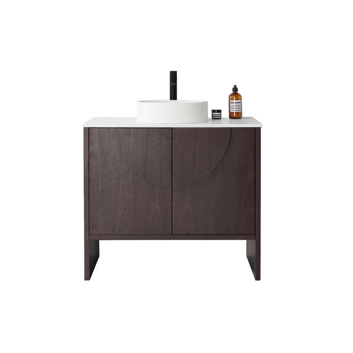 The Celle 36 Inch Bathroom Vanity With Vessel Sink showcases a dark wood cabinet, a white countertop with a round basin, a black faucet, and decorative accents such as a small round container and brown bottle on the right side.