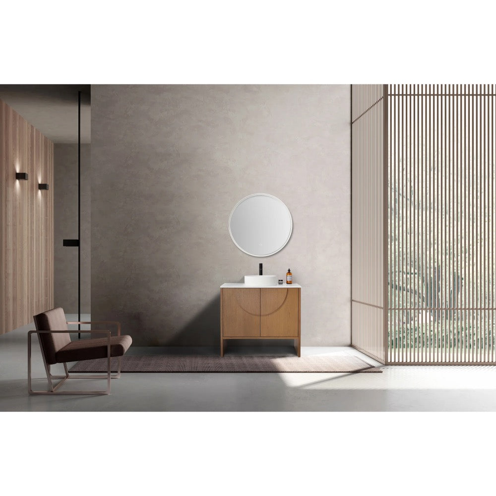 A minimalist bathroom showcases the Celle 36 Inch Bathroom Vanity With Vessel Sink, paired with a round mirror and light grey wall. A modern chair on a rug complements the look, while tall vertical slats frame views of greenery outside.