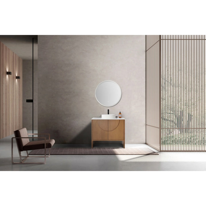 A minimalist bathroom showcases the Celle 36 Inch Bathroom Vanity With Vessel Sink, paired with a round mirror and light grey wall. A modern chair on a rug complements the look, while tall vertical slats frame views of greenery outside.