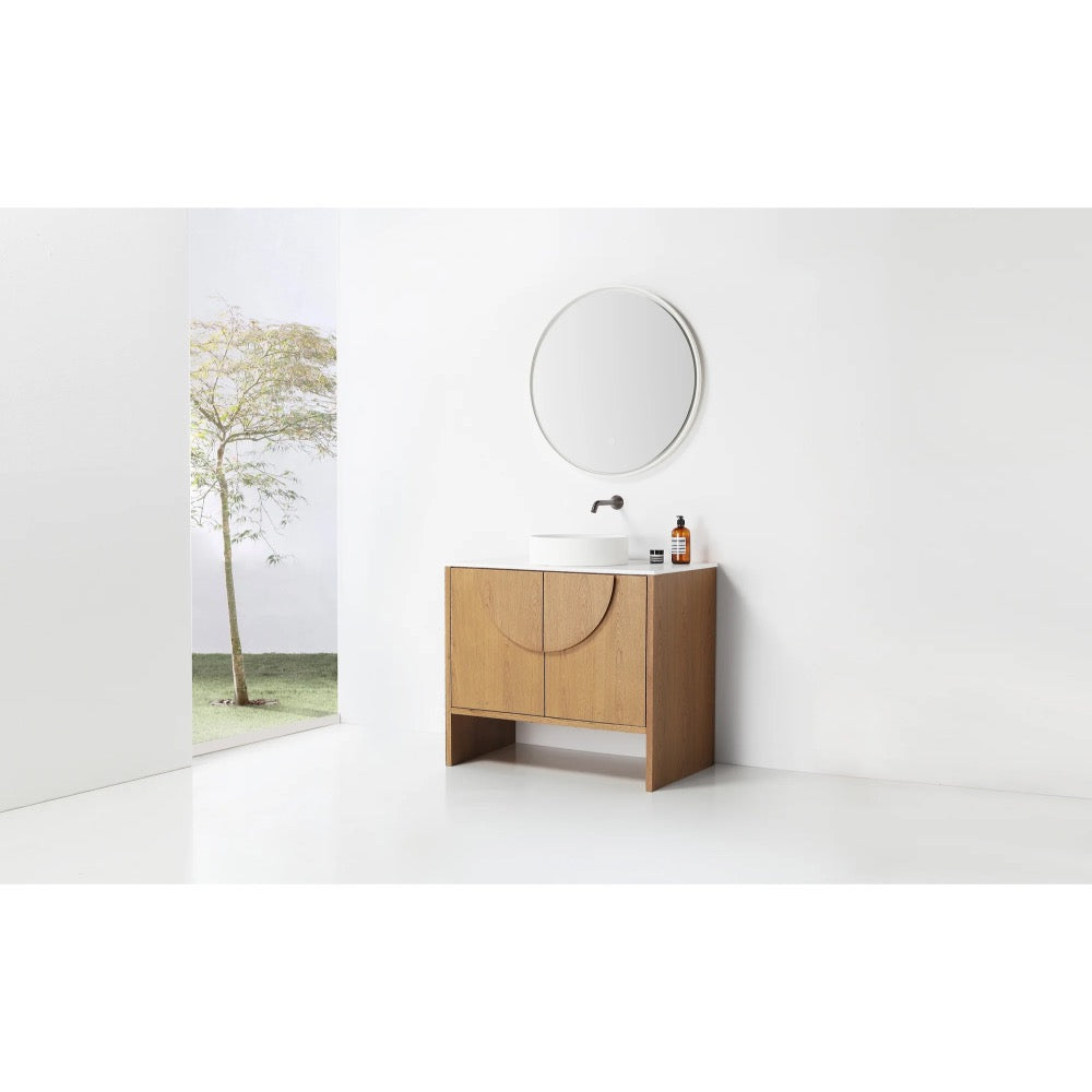 A minimalist bathroom features the Celle 36 Inch Bathroom Vanity With Vessel Sink, a round mirror, and toiletries. A large window showcases a tree and grassy outdoors, filling the space with natural light and an airy vibe.