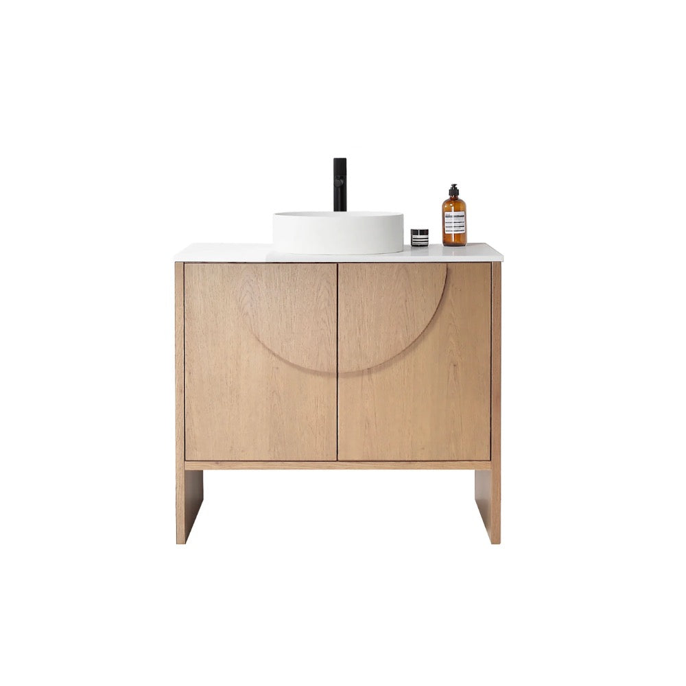 The Celle 36 Inch Bathroom Vanity With Vessel Sink showcases light wood, two doors, a white countertop, a round vessel sink, and a black faucet. A brown bottle and small container are placed on the right side of the countertop.