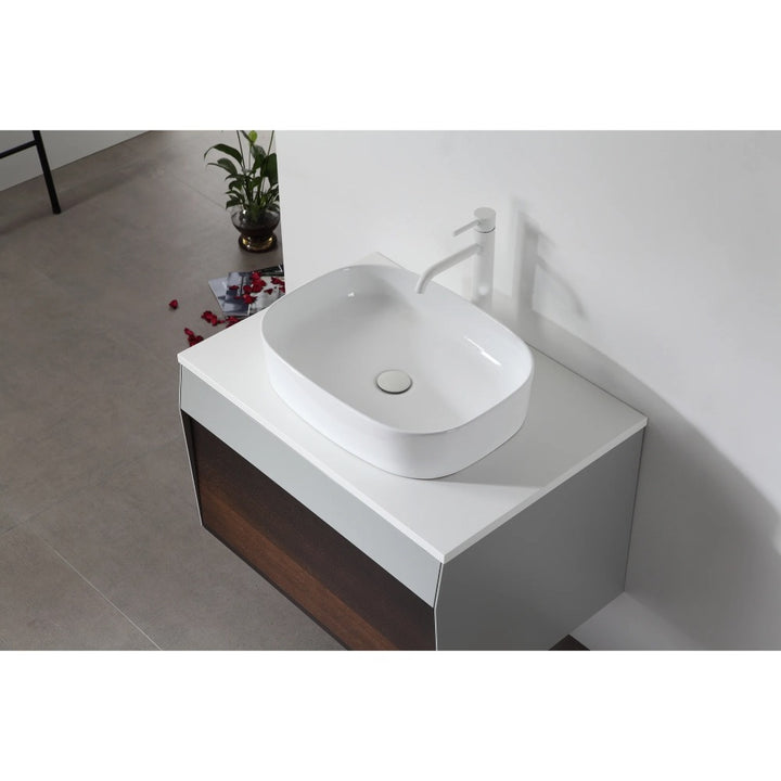A modern white rectangular vessel sink with matching faucet sits atop the Ronda 30 Inch Wall Mount Bathroom Vanity, set against a pristine white wall. Nearby, a small plant and scattered red flower petals add a touch of elegance.
