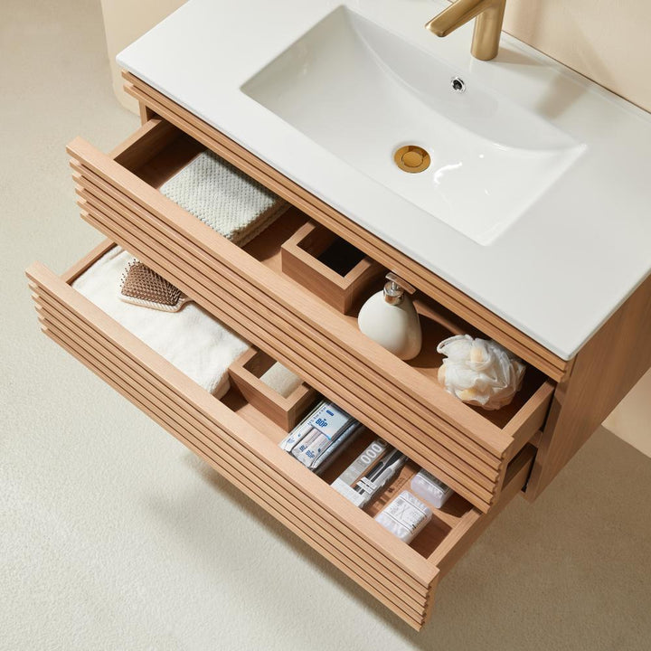 The Linea 36 Inch Wall Mounted Bathroom Vanity features two open wooden drawers, organized with towels, a hairbrush, soap dispensers, toilet paper, and toiletries beneath a white sink with a gold faucet.