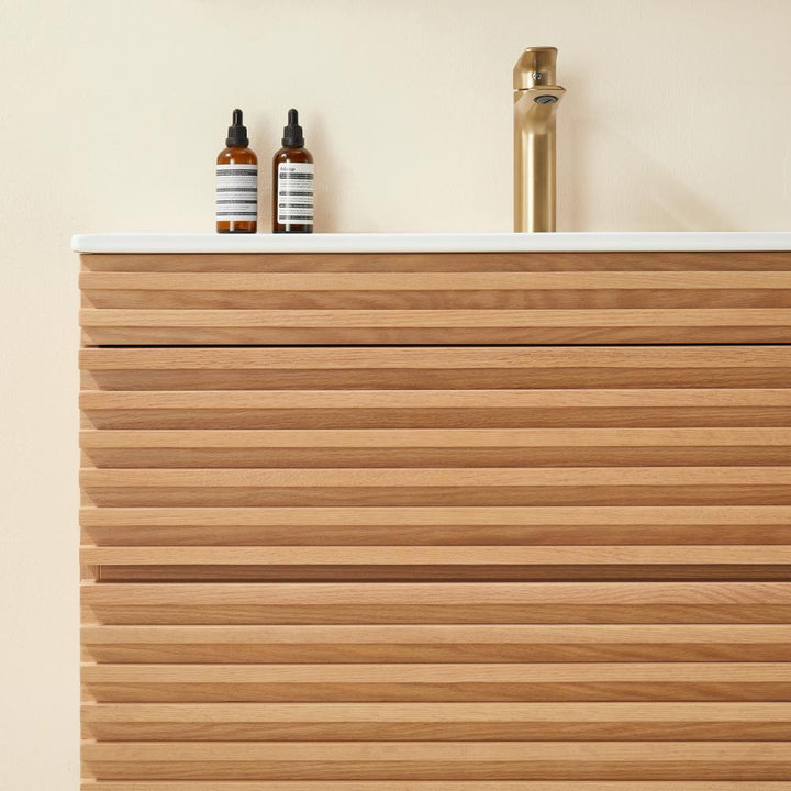 A modern Linea 36 Inch Wall Mounted Bathroom Vanity with horizontal wooden slats, a white countertop, two brown glass bottles with labels, and a gold faucet against a light beige wall.