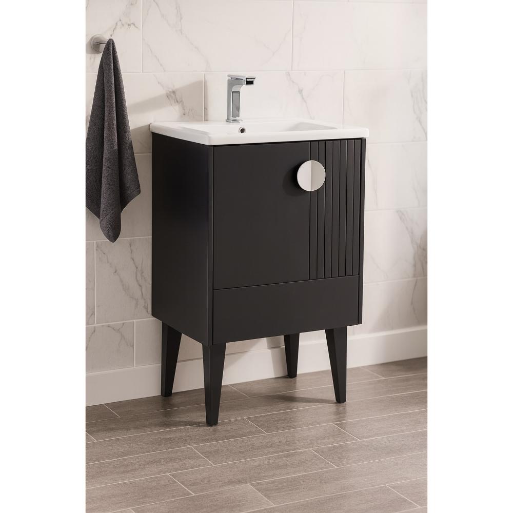 The Venezian 24 inch Bathroom Vanity With Sink in black features tapered legs, a white sink, and a sleek faucet, complemented by a gray towel. White marble tile walls and wood-look floor tiles create a stylish bathroom backdrop.