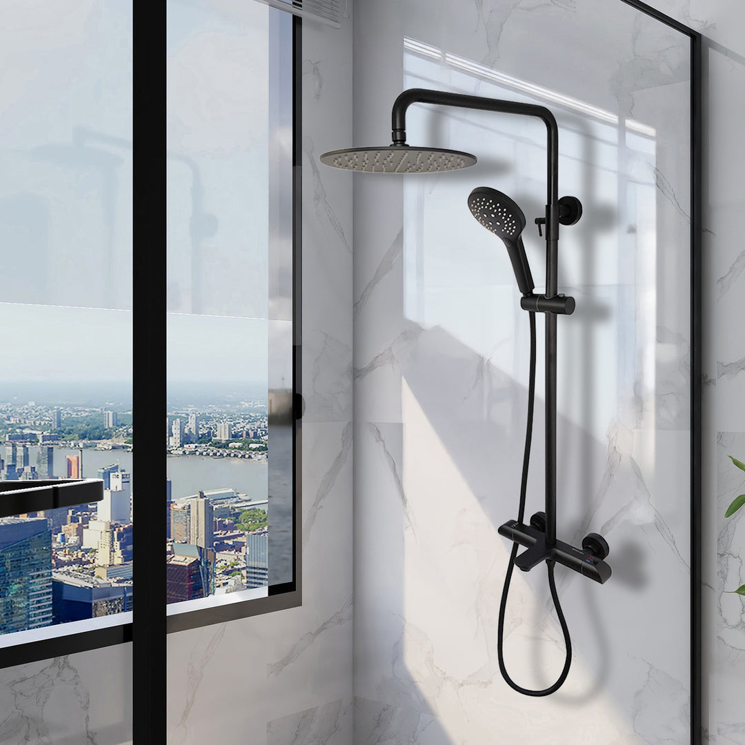The Zen Thermostatic Shower Pipe System, featuring a black rain showerhead and handheld sprayer, is installed on a marble wall beside a large window overlooking the city skyline, tall buildings, and a river.