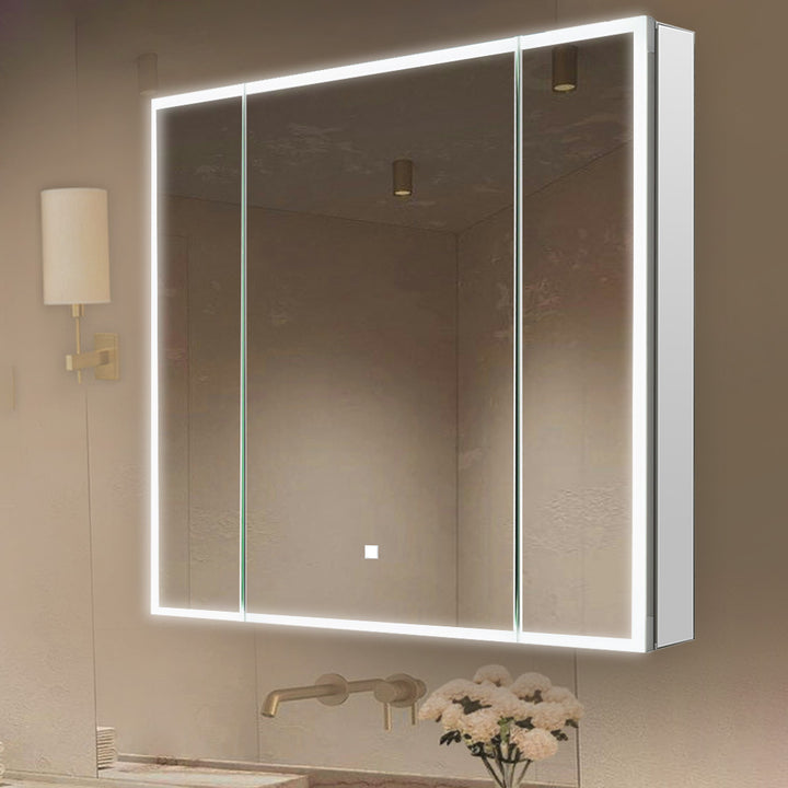 A modern bathroom features the Edge Royal 36 Inch LED Lighted Mirror 3 Door Medicine Cabinet with a spacious rectangular mirror, built-in LED edge lighting, and reflections of the ceiling, lights, and a small white flower vase near the sink.